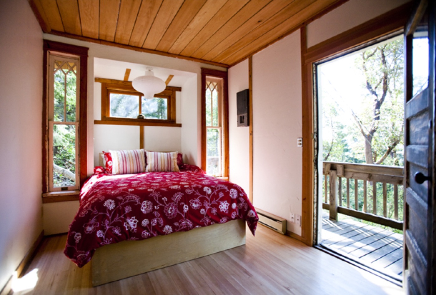 The queen bed under the wood ceiling, deck through the door
